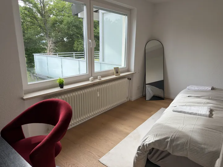 Schlafzimmer mit breitem Fenster, Sessel und Standspiegel