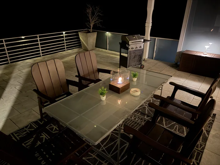 Terrasse am Abend mit Tischfeuer, Holzstühlen und Grill